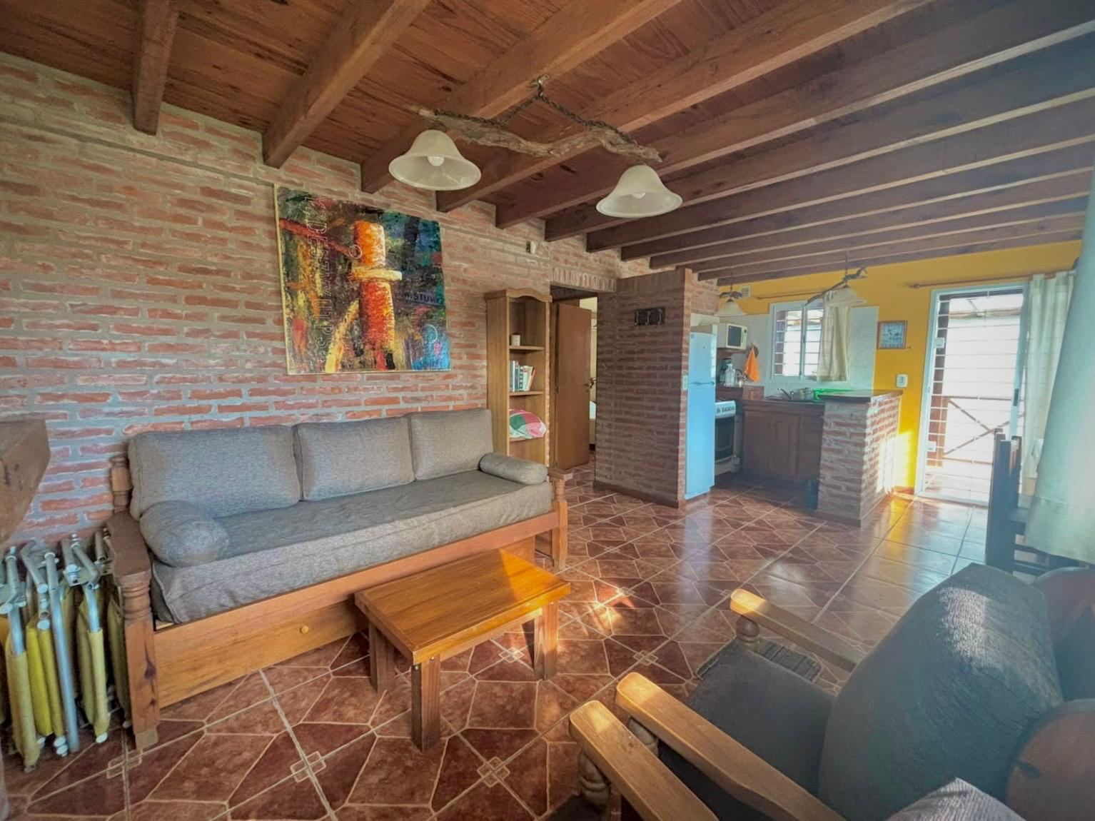 Living con sillón, techo de vigas de madera y cocina integrada