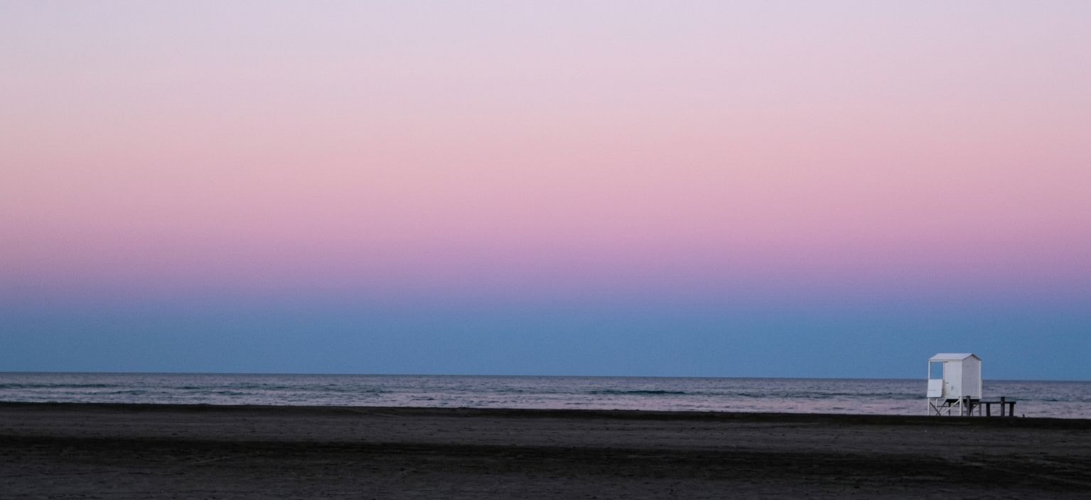 Playa al anochecer con cielo rosa y una casilla de guardavidas